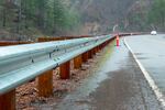 A guardrail along a highway with a view of evergreen trees and slopes in the distance.