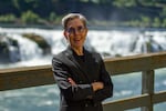 A woman in a suit stands with the Willamette Falls behind her.