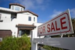 This photo shows a two-story white house for sale in Los Angeles in August 2024. A "For Sale" sign stands in front of the house.