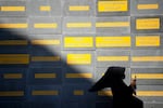 A person holding her phone walks past a wall more than twice her height covered in names.