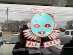 Adhered to the window of Drkmttr Collective's storefront is a sticker of a cartoon angel beaming goofily over the words "all ages."