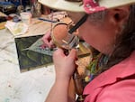 Portland artist Carolyn Garcia applies tiny highlights to a painting using a hand-held magnifying glass.