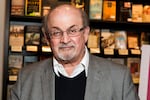 Salman Rushdie poses in front of a row of books
