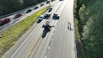 This photo shows an overhead view of State Route 522 in Snohomish County, Washington, after a fatal collision between a Tesla Model S and a motorcycle. The lanes where the collision occurred are shut down, and the Tesla and motorcycle remain at the crash site. First responders and their vehicles stand in the vicinity of the crash site. On the far-left side of the photo, cars drive in an open lane.