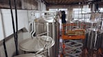 A man pouring hops pellets into a tall steel fermenter.