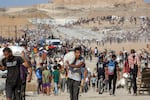 People carry bags of humanitarian aid they received at a distribution center run by the U.S. and Israeli-backed Gaza Humanitarian Foundation (GHF), as they cross the "Netzarim corridor" in the central Gaza Strip, on Aug. 22, while the turrets of Israeli army main battle tanks are pictured in the background.