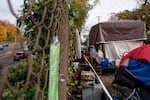 A notice of illegal camping is posted on the fence above a highway as RVs and tents line the street at an encampment of unhoused people in Portland, Ore., on Oct. 31, 2025.