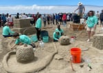 Seven people, most of them in matching shirts, work on sculpting various parts of a pug-themed pumpkin patch, including a pumpkin with the face of a pug, and a wagon covered in hay bales.