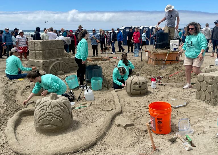 Seven people, most of them in matching shirts, work on sculpting various parts of a pug-themed pumpkin patch, including a pumpkin with the face of a pug, and a wagon covered in hay bales.