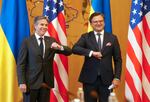 Two men wearing suits smile and bump elbows.