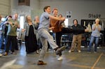 In the foreground, actors Hannah Allen and Noah Cortese hold hands and kick their legs out while dancing during a rehearsal for “Rosie the Riveter the Musical” at Open Space Event Studios in Bend, Ore., June 10, 2026. In the background, from left to right, Blaze Springer, Perry Scott Schwarz, Amy James, Lauren Wray, Trevor Smith, Deena Nororian and Marilyn Magness look on and clap.