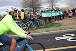 A cyclist rides on the asphalt past a group of people holding a protect our bike lane banner. 