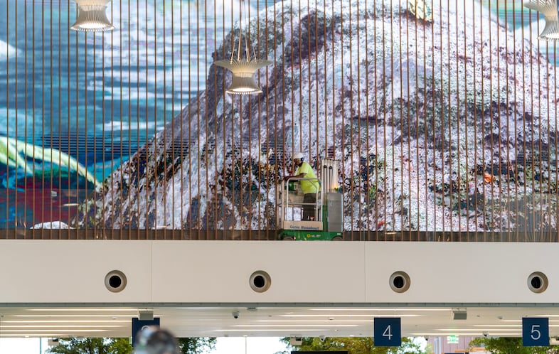 A worker cleans one of the 120-foot-long video walls over the security checkpoint area, Aug. 2, 2024. The two video walls play a 24-hour art installation, “Extraordinary Windows,”  and feature six scenes inspired by regions in the Northwest that are created by three different artists. 