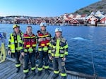 A group of local firefighters pose for a photo in Kungshamn, Sweden, on Sunday, as Hvaldimir swims in the water behind them.