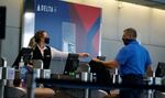 In this July 22, 2020 photo, a ticketing agent for Delta Airlines hands a boarding pass to a passenger as he checks in for a flight in the main terminal of Denver International Airport in Denver.