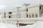 A person walks by homes covered in ice at the waterfront community of Crystal Beach in Fort Erie, Ontario, Canada, on December 28, 2022, following a massive snow storm that knocked out power in the area to thousands of residents.