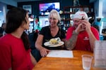 Sharyl Smith, center, owner of Monkey N’Around Pizza, laughs with electricians Micki Bohman, left, and Mark Gruszkiewicz, right, during IBEW Brotherhood Night on Thursday, July 17, 2025, in Quincy, Washington. Bohman and Gruszkiewicz met at a data center job site and got married a year and a half ago.