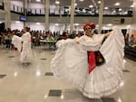 Two dancers in white dresses and skull facepaint lift up the hems of their dresses to dance in a high school common area