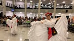 Two dancers in white dresses and skull facepaint lift up the hems of their dresses to dance in a high school common area