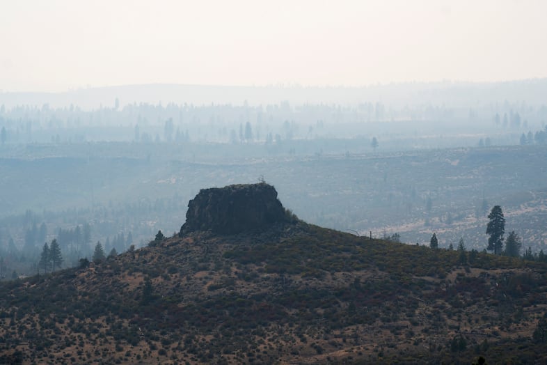 A butte is visible in the foreground, with smoke making the trees and landscape in the background appear hazy and hard to make out.