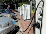 Cars are parked next to vehicle charging stations, while a person stands between two cars and looks around.