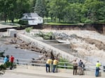 Onlookers take in the catastrophic damage to the Rapidan Dam site in Rapidan, Minn., on Monday. Debris blocked the dam, forcing the heavily backed up waters of the Blue Earth River to reroute along the bank nearest the Dam Store. 
