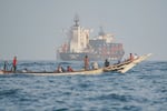 People sail their boat past container ships anchoring near the Strait of Bab al-Mandeb off Yemen's coast in the Gulf of Aden on August 6, 2026.