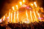 A crowd in front of a concert stage with fire effects shooting up at night.