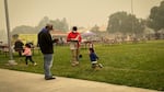 Families stand outside at the Jackson County Expo and read the news as the air is thick with wildfire smoke.