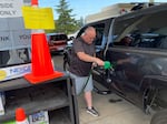 A man pumps has into his pickup truck. To the left, a bright yellow sign reads: "Temporary Self-Serve in effect through Sunday July 31st".