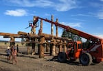 A team uses an all-terrain crane to place a log crossbeam in place on one of the structures that make up the Solar Temple.