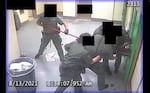 Correctional officers pull a man's arms through a hole in a jail cell door.