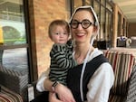 Simone Collins holds her 1-year-old daughter. Collins is wearing round, black-framed glasses and a white bonnet.