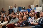 Attendees pack inside the meeting holding signs.
