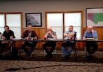 Image of five men sitting at tables during a meeting.
