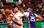 A bearded basketball player in a white Trail Blazers uniform moves the ball towards the hoop as a player in a purple Sacramento Kings uniform tries to block him.