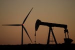 A pumpjack operates in the foreground while a wind turbine at the Buckeye Wind Energy wind farm rises in the distance, Monday, Sept. 30, 2024, near Hays, Kan.