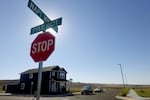 The sun glows behind a stop sign and topped with street signs, one of them stating "Pyaxi Icsit." A two story house with a couple of cars parked in the front are in the background.