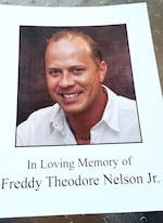A picture of a paper funeral program. The program features the smiling image of a man and the words "In Loving Memory of Freddy Theodore Nelson Jr."