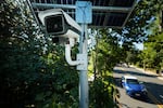 A car drives past an automatic license plate reader that has a camera mounted on a pole to monitor traffic.