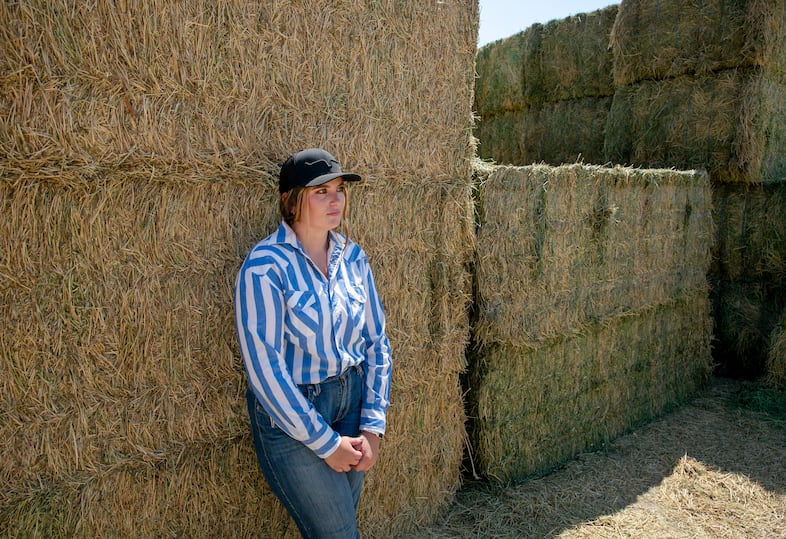 Kyla Wright leans against a tower of hay donated to her family by neighbors. While the Wrights received donations from several neighbors after losing 20,000 acres of grazing land to the Durkee fire, they will still likely be forced to sell some of the cattle they can no longer afford to feed. 