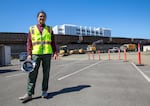 A man stands in a construction site wearing a yellow safety vest, holding a hard hat.