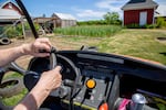 Hands of a woman operating a farm golf cart with a garden in the background.