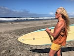 Woman standing on the beach holding a surfboard.