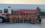 A group of firefighters poses in front of a fire engine.