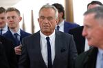 Robert F. Kennedy Jr. is shown walking through a hallway surrounded by men who are likely aides and reporters.
