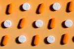 This close-up photo shows rows of pills alternating between acetaminophen (white circular pill) and ibuprofen (orange oval pill) on a bright orange background with a strong shadow.