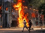 Men run past a shopping center which was set on fire by protesters during a rally against Prime Minister Sheikh Hasina and her government demanding justice for the victims killed in the recent countrywide deadly clashes, in Dhaka, Bangladesh, on Sunday.