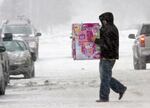 An unidentified person in a dark parka and holding boxes walks across a snowy and icy road between cars in Omaha, Neb., in 2009.