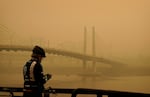 A man stops on his bike along the Willamette River as smoke from wildfires partially obscures the Tilikum Crossing Bridge, Saturday, Sept. 12, 2020, in Portland, Ore.